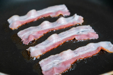 slices of fresh fried bacon in a pan for breakfastの写真素材