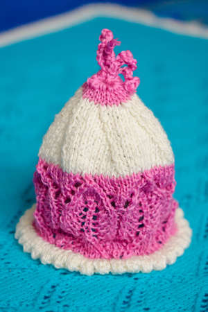 White-pink baby hat, hand-knitted, on a wool background