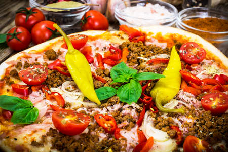 Rustic Italian Pizza on a Thin Pastry with Minced Pork, Ham, Tomatoes, Hot Peppers and Basil. Street Fast Food. Studio Photoの写真素材