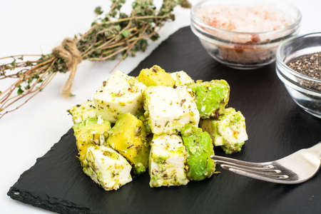 Appetizer with avocado and cheese with herbs on black stone