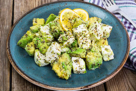 Salad with goat cheese, avocado and olive oil on wood background