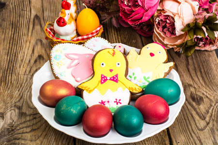 Easter colored eggs and cakes with icing on white plateの写真素材