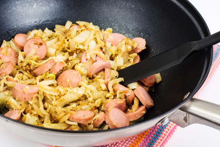 Stewed cabbage with sausages in frying pan over white backgroundの写真素材