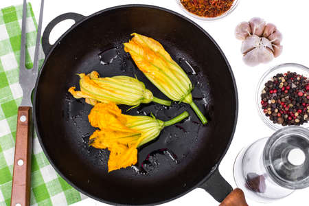 Yellow pumpkin flowers and zucchini in frying pan for cookingの写真素材