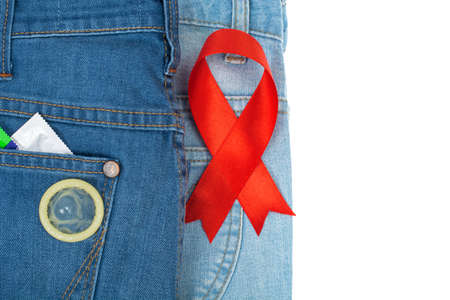 Red ribbon and condom on blue jeans background. Concept of awareness and protection against AIDS,...