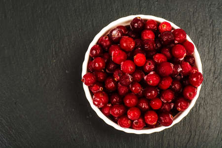 Frozen berries of cranberries in white bowl on black stone. Studio Photo