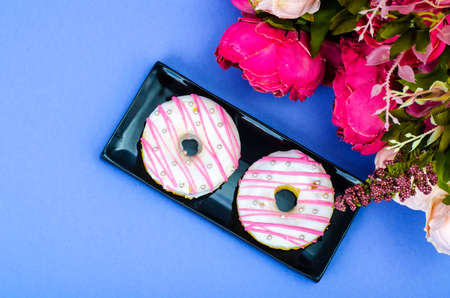 Two fresh round donuts on black plate