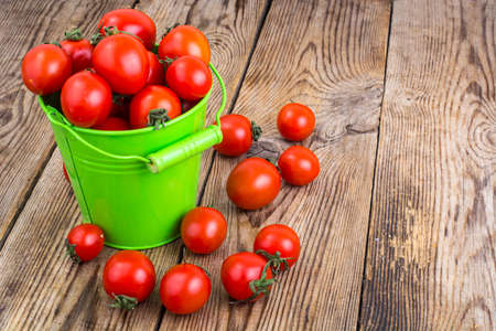 Cherry tomatoes harvest in green bucket on wooden table. Studio Photo
の写真素材