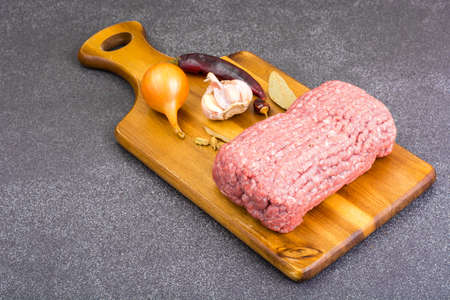 Fresh ground meat on wooden board with spices, vegetables