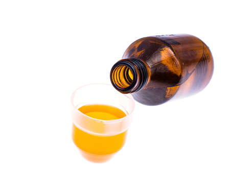 Medical bottle and measuring plastic cup with medicinal syrup on white backgroundの写真素材