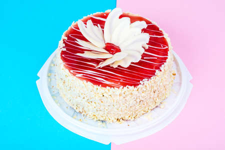 Homemade cake with red icing and white chocolate on bright colored background. Studio Photo