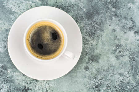White cup with black espresso coffee on blue and gray background