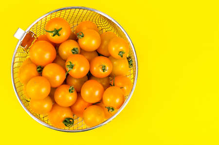Yellow ripe small tomatoes in metal basket.