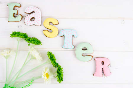 Creative greeting Happy Easter. Lettering from biscuits on white wooden background. Pastel holiday...