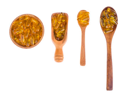 Yellow vitamin soft gelatin pills in wooden bowl, spoons and scoop on white background.の写真素材