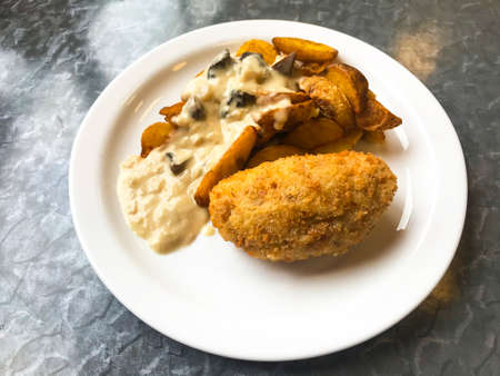 Potato wedges with mushroom sauce, cutlet on plate.