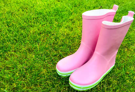 Pink rubber boots stand on green grass. Studio Photo