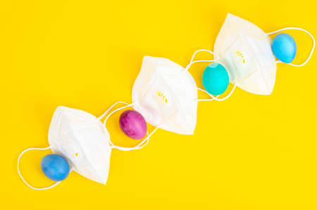 Concept of quarantine at Easter. Decorative eggs and white protective masks on bright background. Social distancing. Studio Photoの写真素材