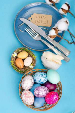 Festive Easter table setting with painted eggs on blue background. Space for text. photo