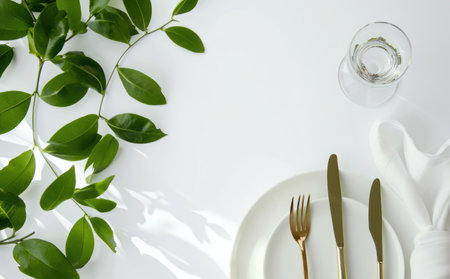 white table setting with green plant leaves.の素材