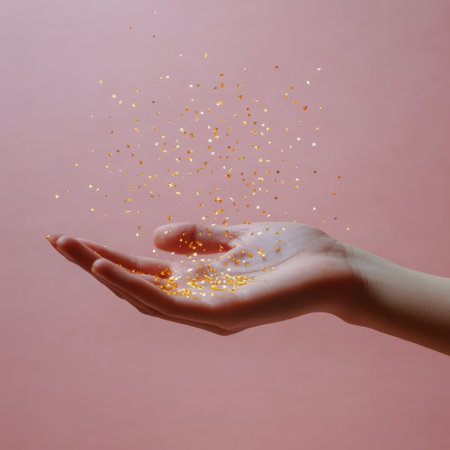 A hand extends gracefully, letting tiny golden particles drift through the air against a smooth pink backdrop. The shimmering effect creates a whimsical atmosphere, capturing a fleeting moment of enchantment and wonder.の素材