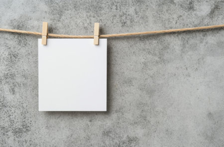 A blank white sheet is clipped with wooden clothespins, suspended from twine against a textured gray wall, creating a simple, minimalist aesthetic for notes or creativity.の素材