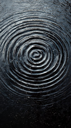 Circular ripples appear in dark water as raindrops fall, creating a soothing visual effect. The quietness of the surroundings adds to the peaceful ambiance.の素材
