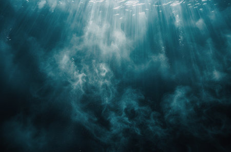 Sunbeams shine through the surface of blue ocean water, illuminating the dark depths and illuminating a rocky seabed.の素材
