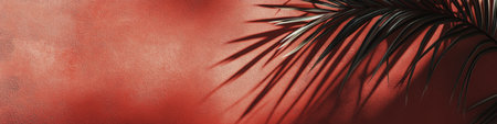 Soft shadows of palm leaves stretch across a bright red wall, creating an artistic interplay of light and dark in a serene afternoon setting. The tropical feel enhances the ambiance.の素材