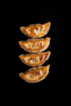 A delicious display of seven golden brown dumplings arranged in a vertical line. The crispy texture shines against the simple black background, highlighting their appetizing appearance.の素材