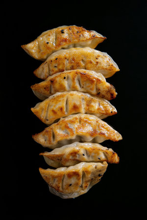A delicious display of seven golden brown dumplings arranged in a vertical line. The crispy texture shines against the simple black background, highlighting their appetizing appearance.の素材