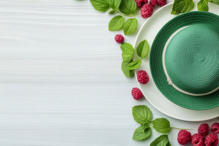 A vibrant green straw hat is placed on a white wooden table, surrounded by fresh raspberries and mint leaves, creating a cheerful and refreshing summer ambiance.の素材