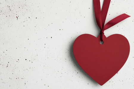 A red heart shaped ornament dangles from a black ribbon against a textured white wooden background, creating a simple yet charming decorative element suitable for various occasions.の素材