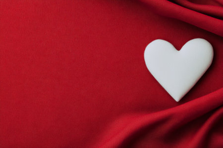 A warm red fabric serves as the backdrop, complemented by a white heart shape resting beside a textured red knit blanket. This arrangement evokes feelings of love and comfort.の素材