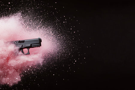 A black handgun is surrounded by a vibrant cloud of pink powder, creating a striking contrast against a dark background. The dramatic effect emphasizes both the weapon and the explosion of color.の素材