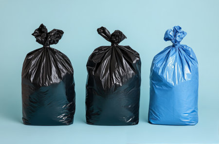 Three garbage bags in varying colors stand against a bright blue background. The bags represent waste management practices, indicating a focus on recycling and organization.の素材