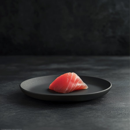 Freshly cut tuna cubes arranged neatly on a textured black plate. The vibrant color of the tuna stands out against the dark background, highlighting the quality of the fish.の素材