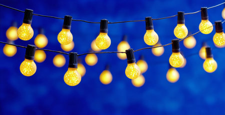 A collection of yellow light bulbs hangs gracefully against a vivid blue background, creating a warm and inviting atmosphere perfect for celebrations or gatherings.の素材