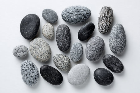 A collection of smooth stones displayed on a light surface. The stones vary in color and size, creating an interesting arrangement. Some stones are dark, while others are light or gray..の素材