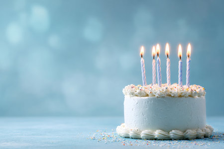 A decorated white cake sits on a blue table with five lit candles on top. Colorful sprinkles surround the cake, adding a festive touch for a celebration or birthday party.の素材