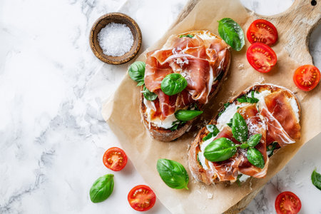 Freshly made bruschetta topped with layers of prosciutto, creamy mozzarella, and aromatic basil, arranged beautifully with cherry tomatoes on a wooden board.の素材