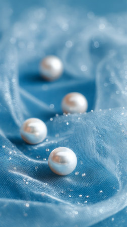 Pearls lie gracefully on light blue fabric, surrounded by shimmering sparkles. The soft texture adds an elegant touch to the tranquil arrangement.の素材
