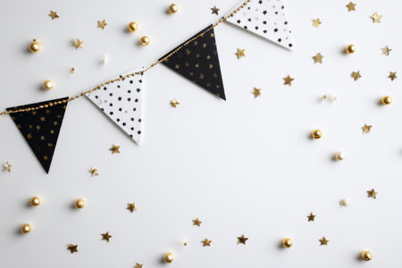 Colorful bunting in black and white hangs across a white surface, surrounded by golden stars and ornaments, creating a cheerful and celebratory atmosphere.の素材
