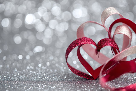 Colorful ribbons shaped like hearts are arranged on a sparkling silver surface, creating a cheerful and festive vibe perfect for celebrations or romantic occasions.の素材