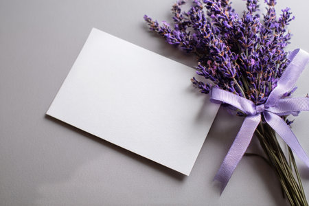 A bundle of fresh lavender tied with a purple ribbon sits next to a blank card on a smooth gray surface, perfect for personal notes or special occasions.の素材