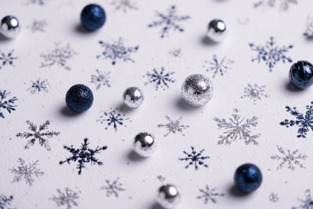 Colorful blue and silver ornaments lay on a white surface, surrounded by delicate snowflakes. This festive scene captures the spirit of winter and holiday cheer..の素材