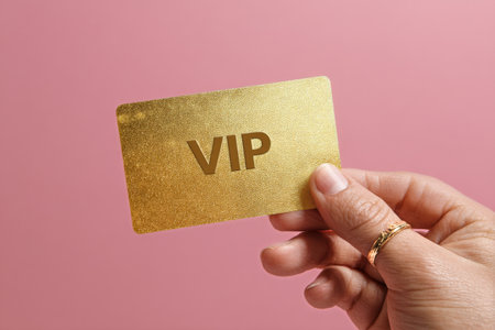 A hand holds a shiny golden VIP card with bold letters against a soft pink background, symbolizing exclusivity and special privileges in events or services.の素材