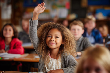 A smiling child with curly hair raises her hand in a classroom filled with attentive classmates. The setting is focused on learning and participation among students.の素材