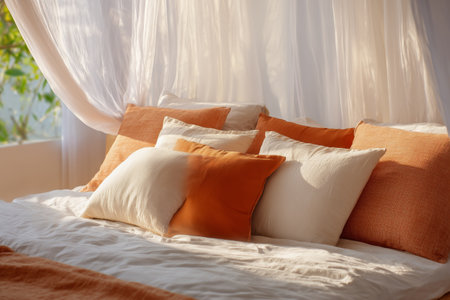 Soft pillows in shades of peach and cream adorn a neatly made bed. Sunlight filters through sheer curtains, creating a warm and inviting atmosphere in the bedroom.の素材