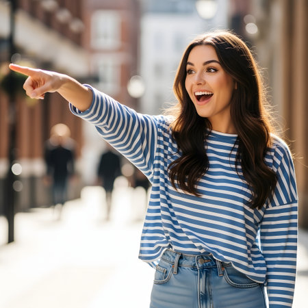 happy young woman pointing with finger at something on city street in summerの素材